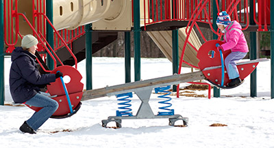 A mom and daughter are on the seesaw at the snowy park.