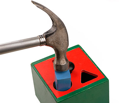 A hammer literally trying to force a square peg into a round hole.